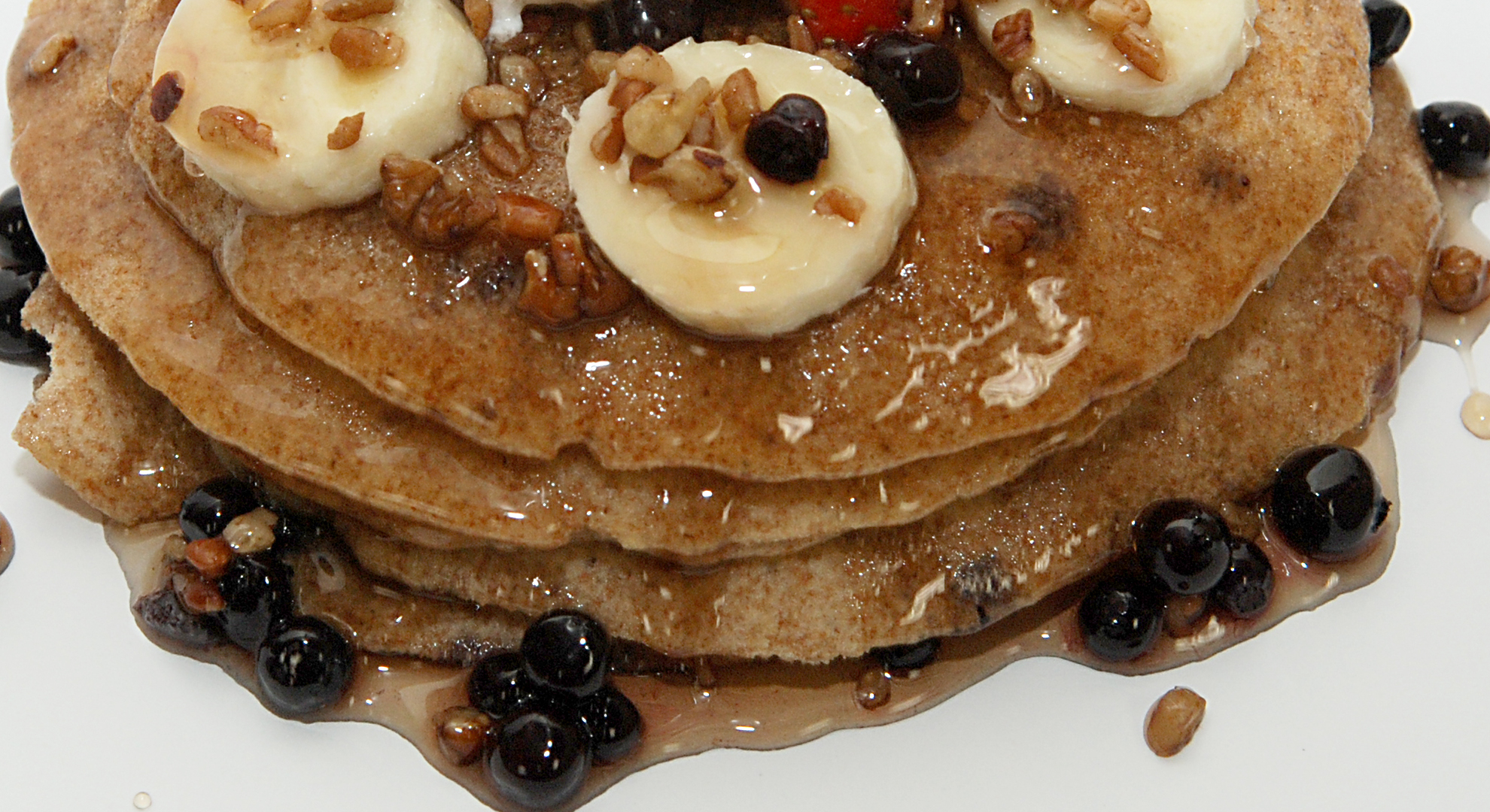 Whole wheat pancakes with bananas, blueberries and pecans dripping with syrup.